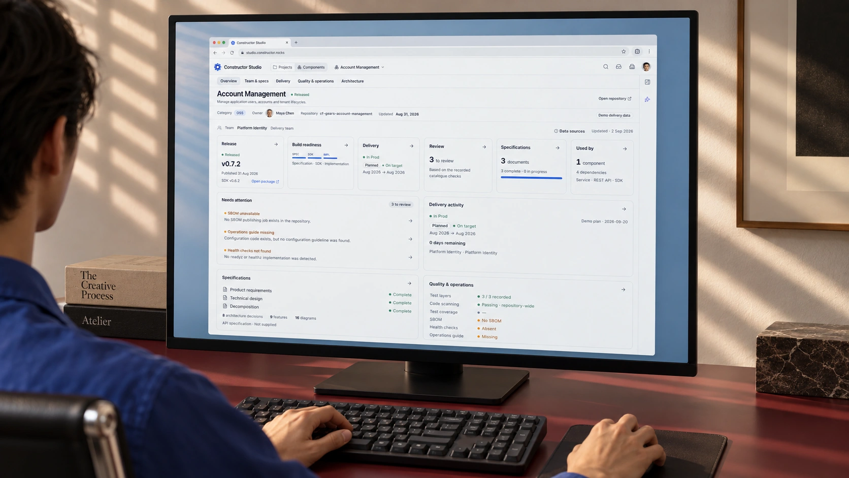 Constructor Fabric workspace in a browser window on a monitor facing a seated designer, with a burgundy desk and striped daylight