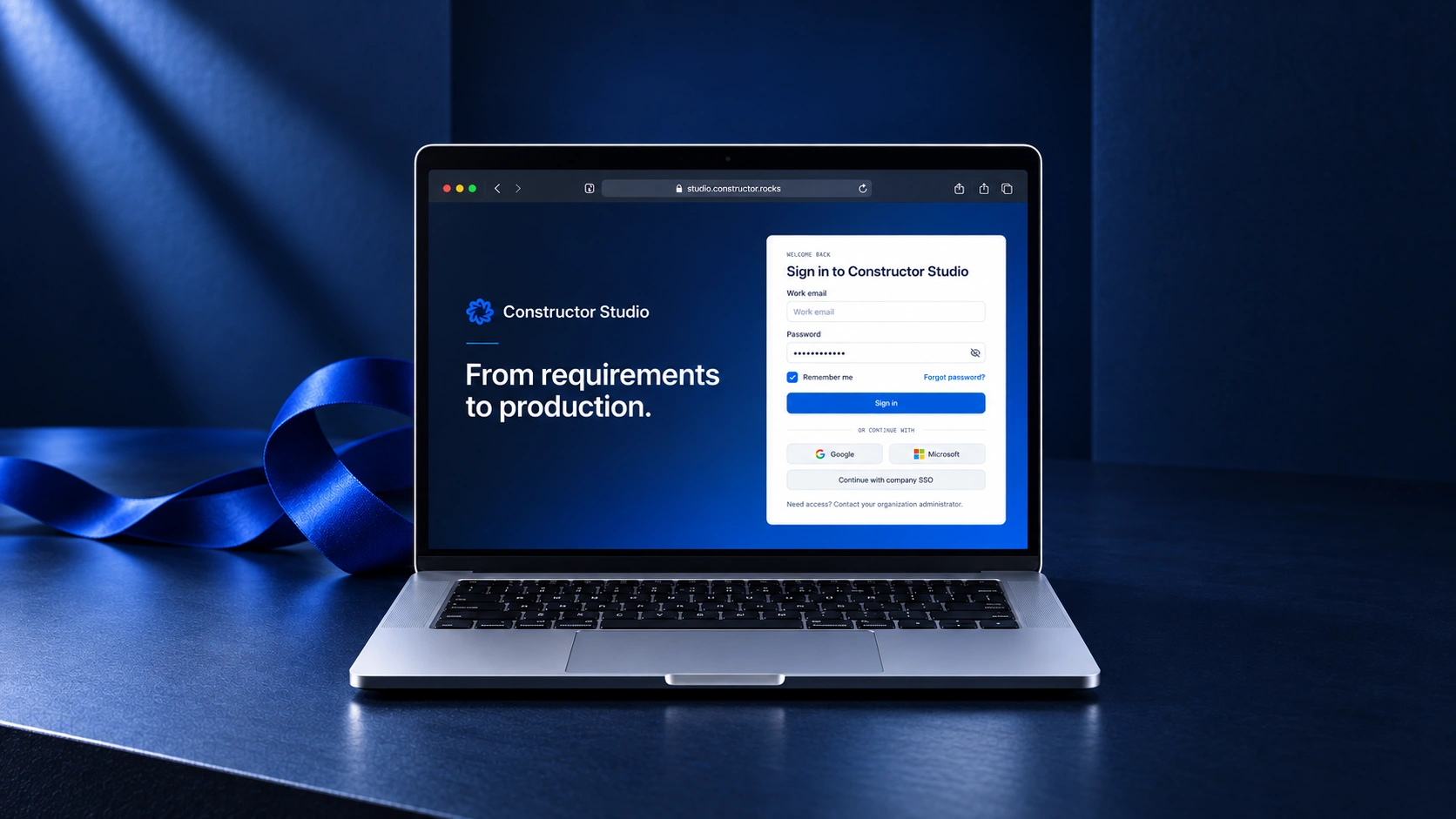 Constructor Fabric: a laptop displaying the Studio sign-in screen beside a cobalt ribbon in a dark blue studio